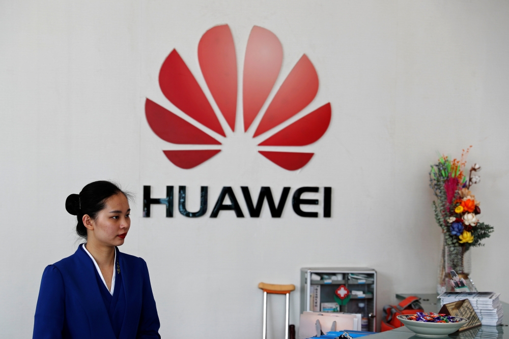An employee stands next to the logo of Huawei in Shenzhen, Guangdong province, China March 29, 2019. Reuters/Tyrone Siu