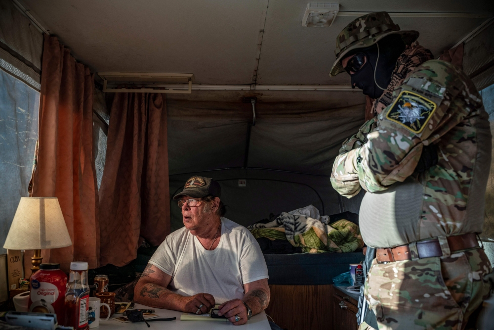 (FILES) In this file photo taken on March 20, 2019 Striker (L), the leader of the Constitutional Patriots New Mexico Border Ops Team militia, speaks with Viper (R), who go by aliases to protect their identity, inside the team's camper while discussing log