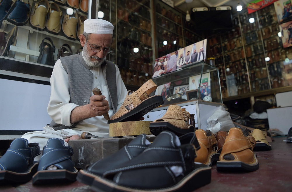 In this picture taken on April 1, 2019, Chacha Noor Din, the owner of a string of shoe stores, makes a pair of sandals at his shop in Peshawar.  AFP / Abdul Majeed
