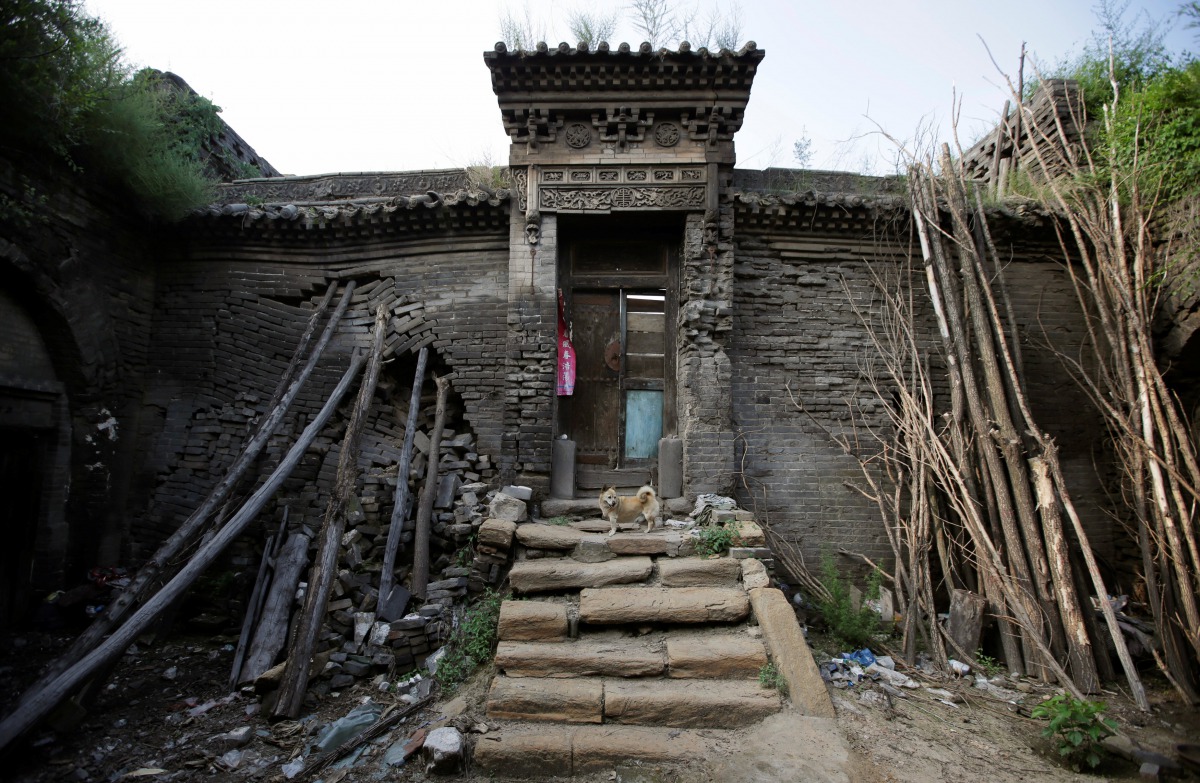 Tree trunks and rocks are set up to support a leaning wall of damaged cave house in an area where land is sinking next to a coal mine in Helin village of Xiaoyi, Shanxi province, China, August 2, 2016. Reuters 