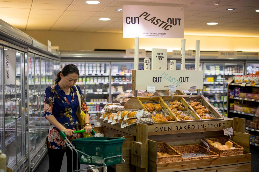 Signs promoting plastic free packaging are seen above a display of loose fresh fruit as a shopper browses at Budgens supermarket in Belsize Park, north London on July 2, 2019. AFP / TOLGA AKMEN 