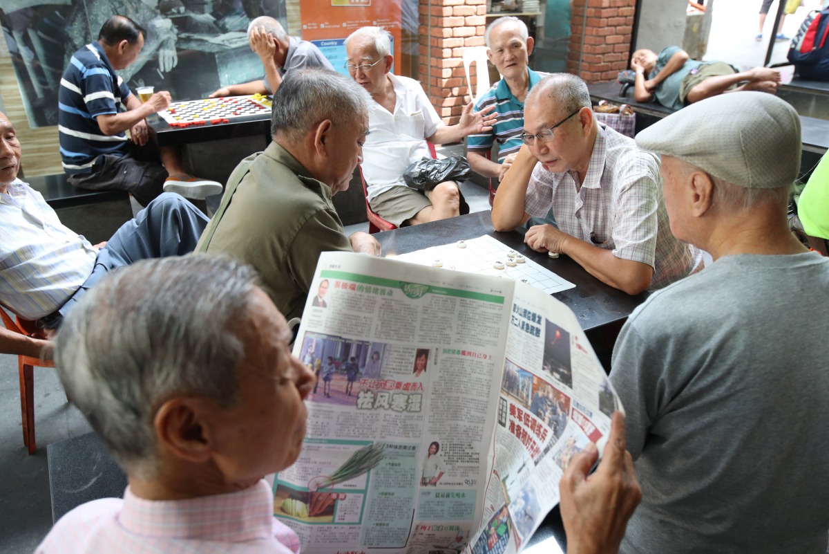A man reads a newspaper as others play checkers in Singapore, January 16, 2018. Reuters/Calvin Wong