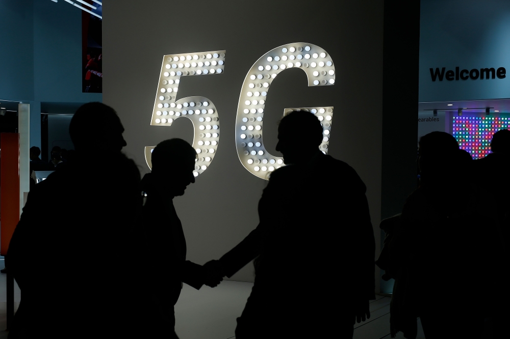 Visitors shake hands next to a 5G hotspot sign at the Mobile World Congress in Barcelona on February 27, 2019. AFP / Pau Barrena