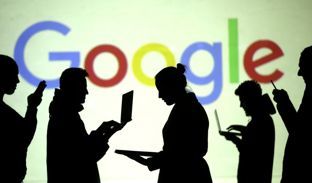 Silhouettes of laptop and mobile device users are seen next to a screen projection of Google logo in this picture illustration taken March 28, 2018. Reuters / Dado Ruvic