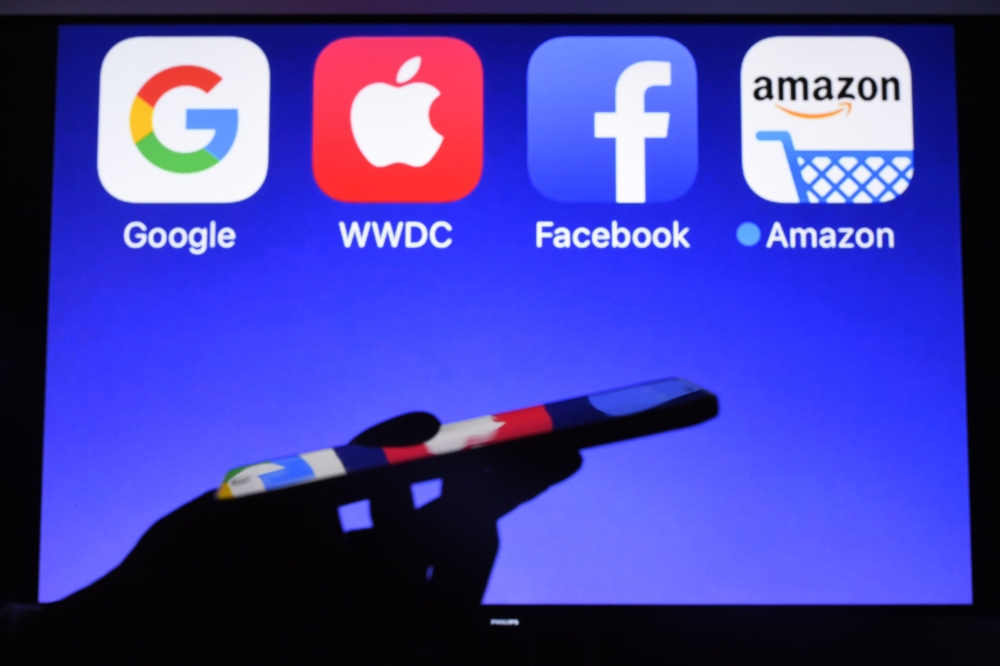 A smartphone being operated in front of GAFA logos,  acronym for Google Apple Facebook and Amazon, as background in Hédé-Bazouges, western France, on September 28, 2017. AFP / Damien Meyer