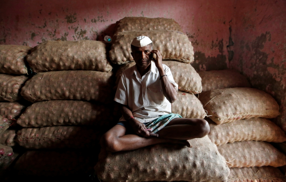 A labourer talks on his mobile phone as he sits on sacks of onions at a wholesale market in Mumbai, India February 15, 2018. Reuters/Francis Mascarenhas