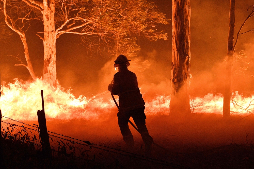 A firefighter hosing down trees and flying embers in an effort to secure nearby houses from bushfires near Nowra tow New South Wales, Australia, December 31, 2019. AFP / Saeed Khan