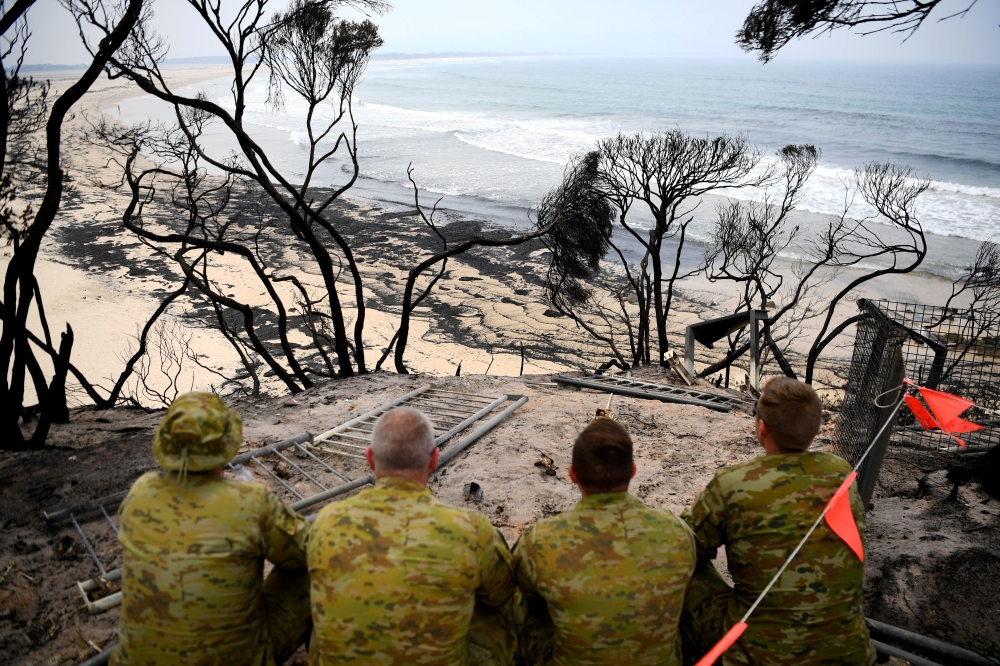 Soldiers sit on a beach amongst burnt trees where people had previously taken shelter during a fire on New Year's Eve in Mallacoota, Australia January 10, 2020. Reuters/Tracey Nearmy
 