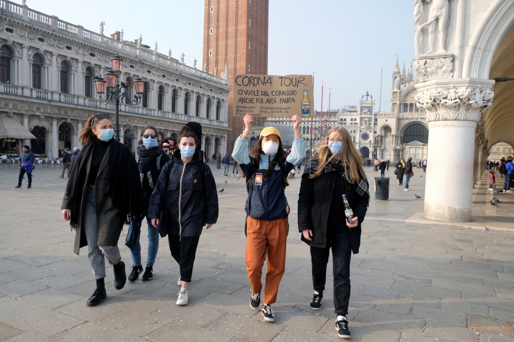 People wear protective face masks as they walk in St. Mark's square holding a placard that reads 