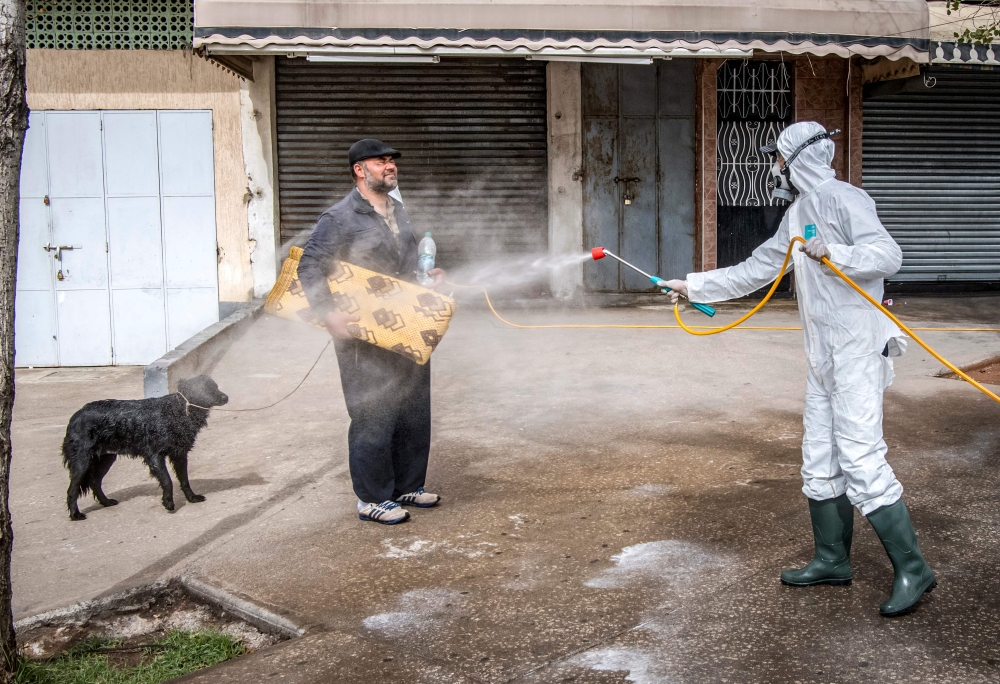 A Moroccan health ministry worker disinfects a man walking a dog and carrying a mat in the capital Rabat on March 22, 2020. AFP / Fadel Senna
 