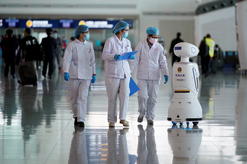 Medical workers walk by a police Robot at the Wuhan Tianhe International Airport after travel restrictions to leave Wuhan, the capital of Hubei province and China's epicentre of the novel coronavirus disease (COVID-19) outbreak, were lifted, April 8, 2020