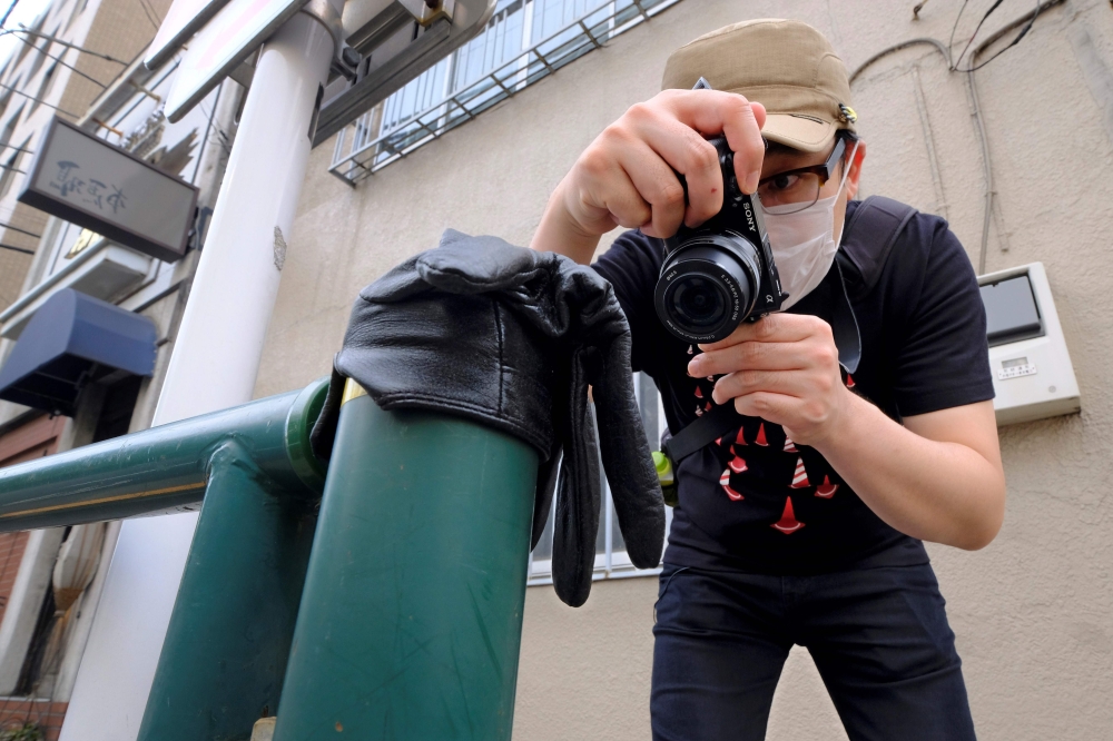 This picture taken on May 25, 2020 shows Japanese photographer Koji Ishii taking pictures of a lost glove on a pole beside the road in Tokyo. AFP / Kazuhiro Nogi 