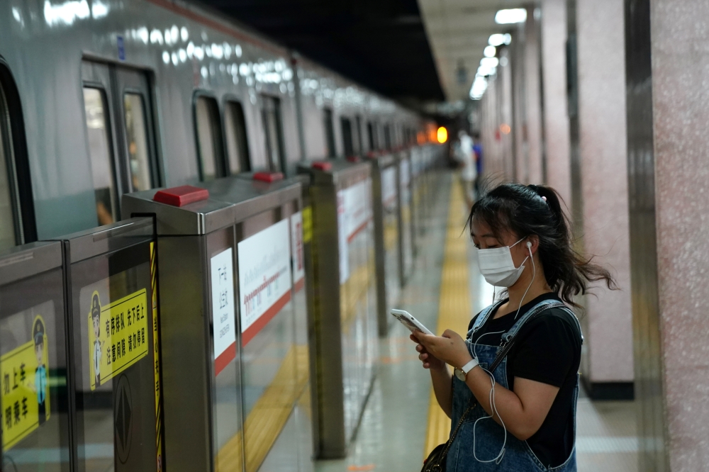 A woman wearing a face mask following the coronavirus disease (COVID-19) outbreak looks at her smartphone while waiting for a subway in Beijing, China August 11, 2020. REUTERS/Tingshu Wang