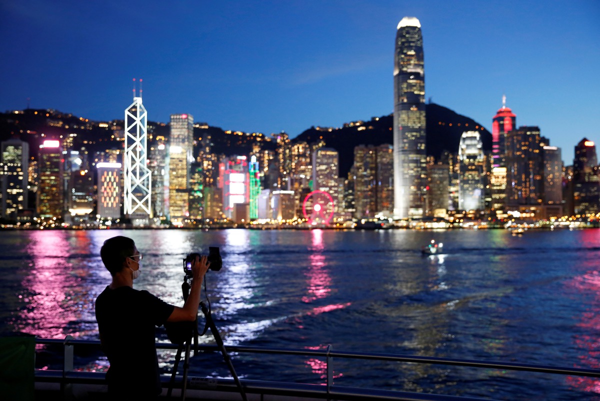 FILE PHOTO: A man wearing a protective face mask takes a photo of the sunset at Tsim Sha Tsui waterfront as skyline buildings stand across Victoria Harbor following the coronavirus disease (COVID-19) outbreak in Hong Kong, China July 28, 2020. REUTERS/Tyr