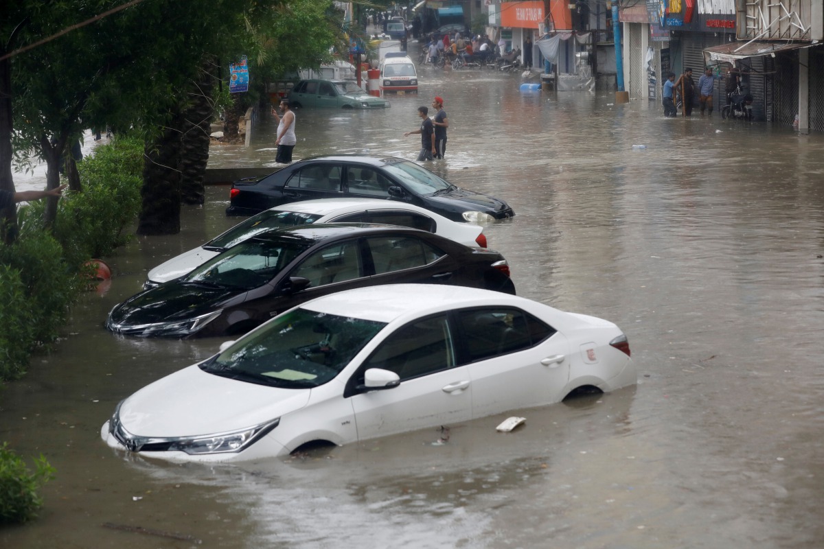 People wade through a flooded street with submerged vehicles during the monsoon rain, as the outbreak of the coronavirus disease (COVID-19) continues, in Karachi, Pakistan August 25, 2020. REUTERS/Akhtar Soomro
