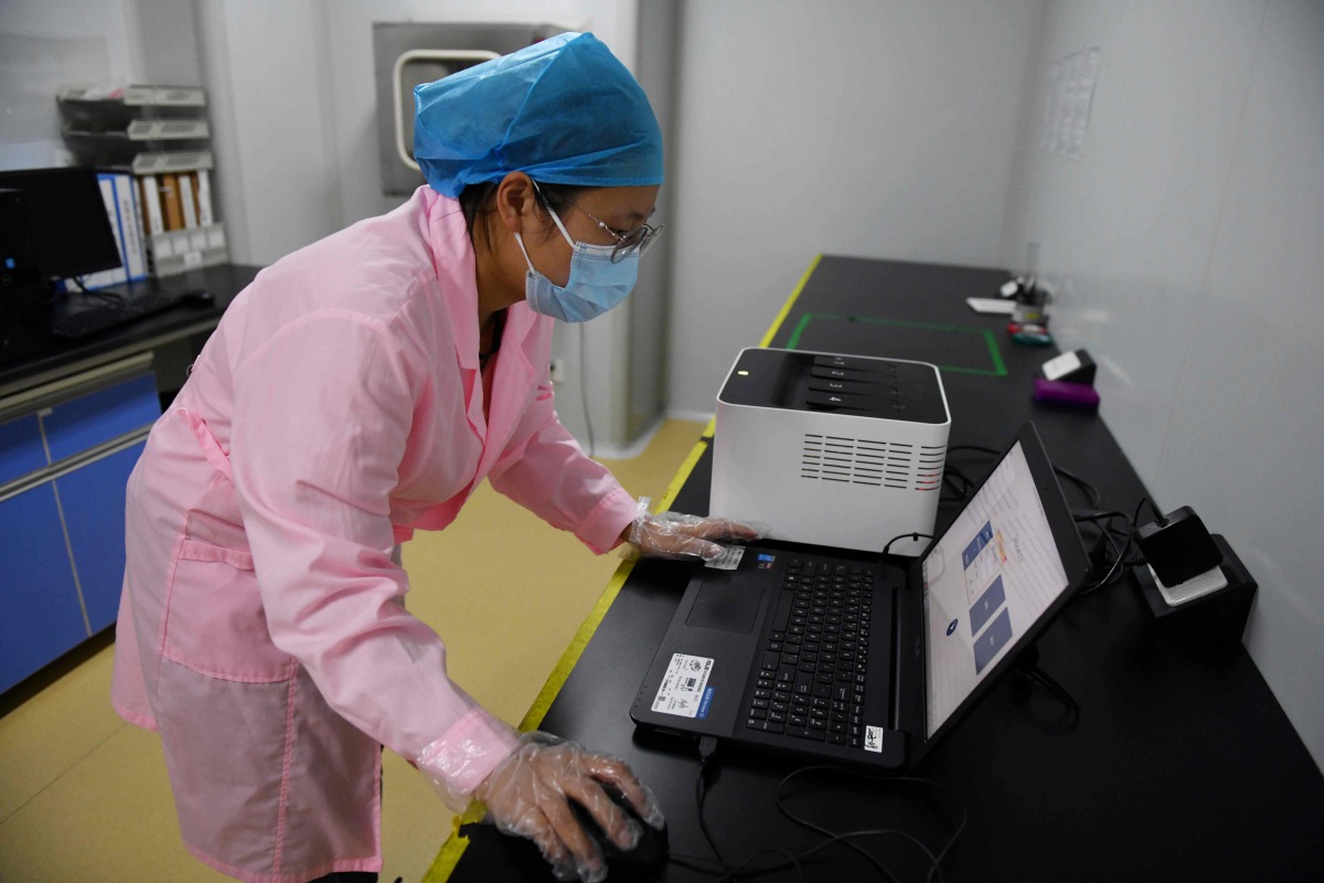 This photo taken on September 27, 2020 shows a technician in Beijing checking test results using the Flash 20 (at rear), a machine developed by Chinese biotech company Coyote as a fast test for the COVID-19 coronavirus. / AFP / GREG BAKER
