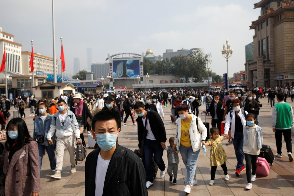 People wearing masks following the coronavirus disease (COVID-19) outbreak are seen with luggage outside Beijing Railway Station, during the holidays of Mid-Autumn Festival and National Day, in China October 1, 2020. REUTERS/Carlos Garcia Rawlins