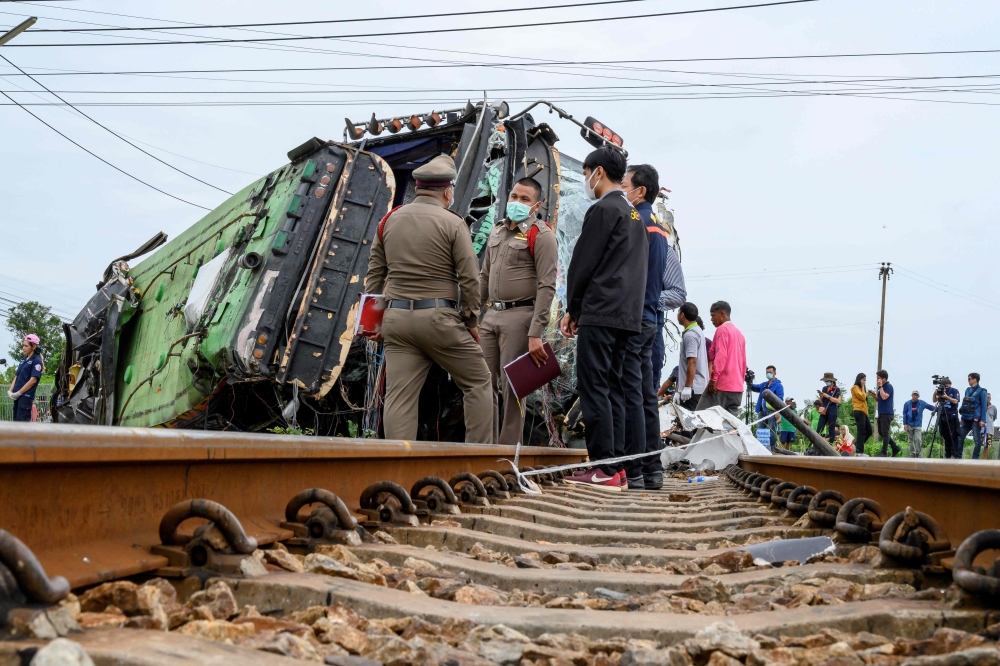Investigators work by the wreckage of an overturned bus involved in a deadly collision with a train next to Khlong Kwaeng Klan railway station in Chachoengsao province, east of the Thai capital Bangkok, on October 11, 2020. / AFP / Mladen ANTONOV