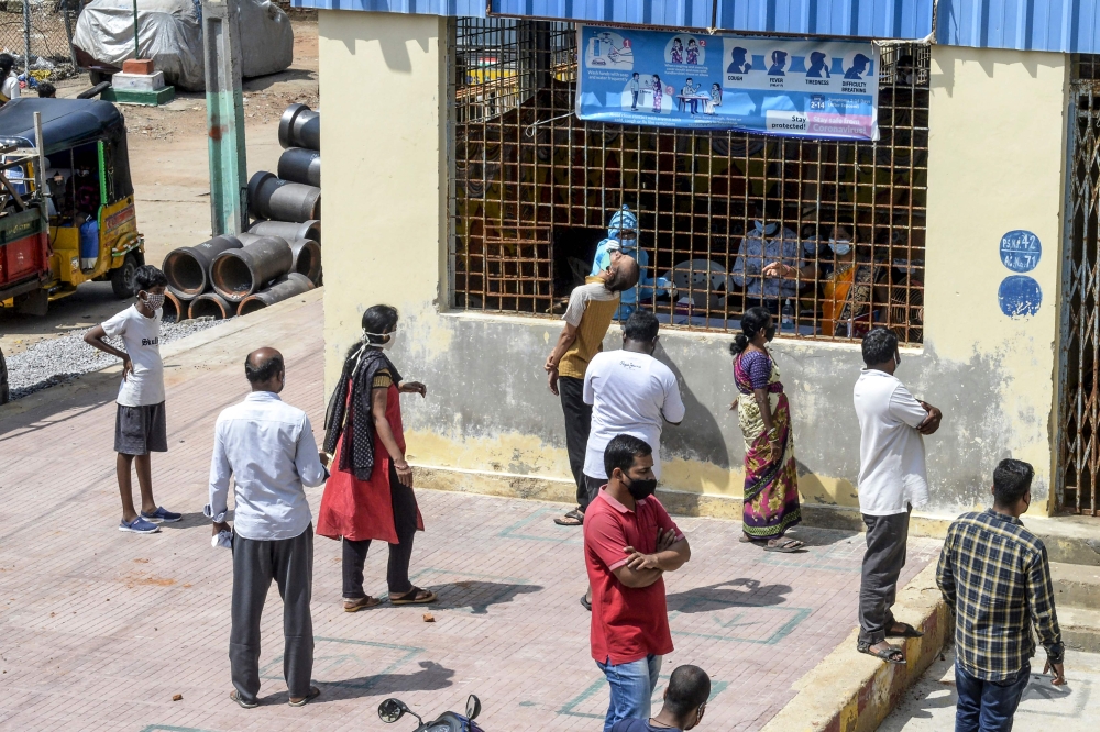 Residents wait as a health worker (C background) collects a swab sample from a man to test for the Covid-19 coronavirus before going to a medical camp for flood victims at a slum area following heavy rains in Hyderabad on October 16, 2020. AFP / NOAH SEEL