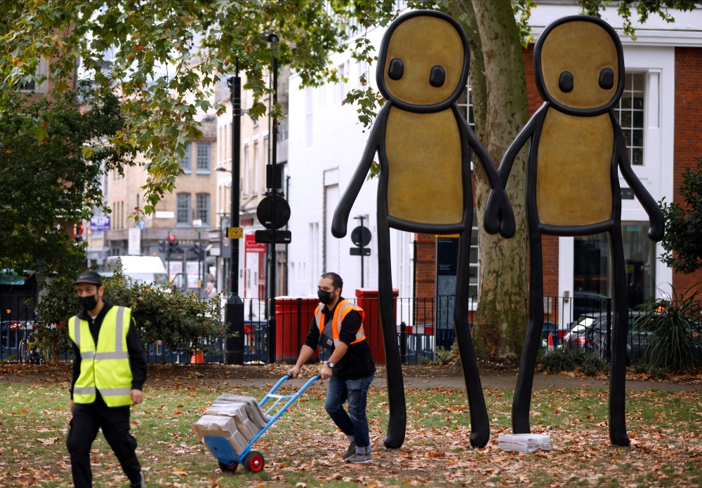 Staff working for British street artist STIK move bundles of local newspapers containing free copies of his artwork to be given away to local residents, during the unveiling of his bronze sculpture 