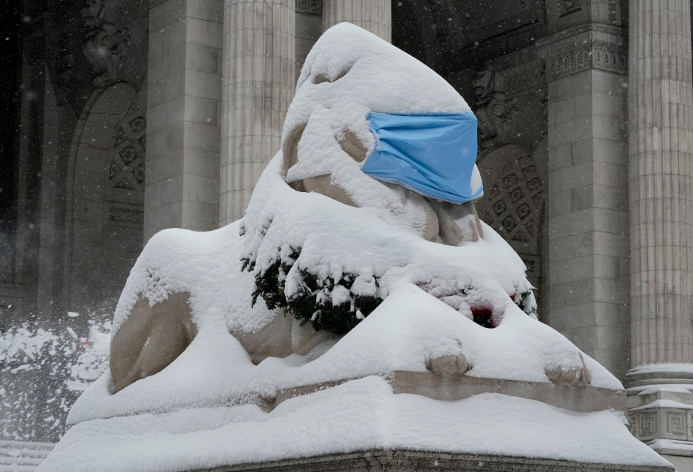 The lion statue named Patience, located outside the Fifth Avenue and East 42nd Street branch of the New York Public Library, is adorned with a facemask and covered in snow on December 17, 2020 in New York ( AFP / TIMOTHY A. CLARY)
