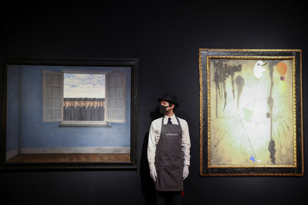 A gallery assistant stands next to artwork titled 'Le Mois des Vendanges' by Rene Magritte and 'Peinture' by Joan Miro, during a photocall at Christie's auction house, in London, Britain, March 16, 2021. The items are to go on sale at the forthcoming 20th