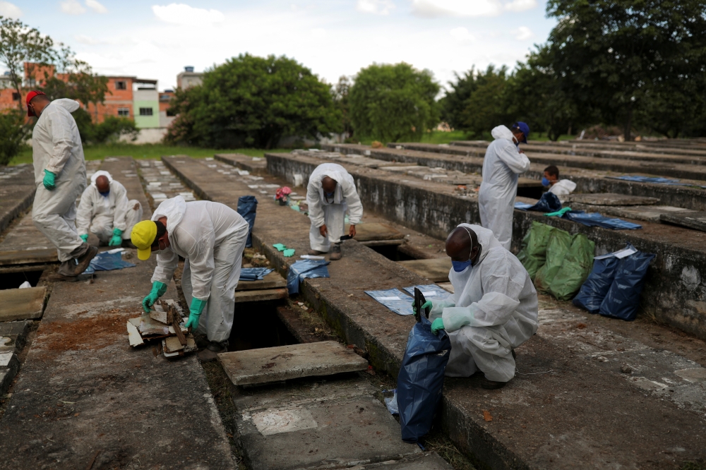 Gravediggers wearing protective suits close bags with bones during exhumations to open space on cement graves as new burials are suspended, except private deposits and children, at Vila Nova Cachoeirinha cemetery amid the outbreak of the coronavirus disea