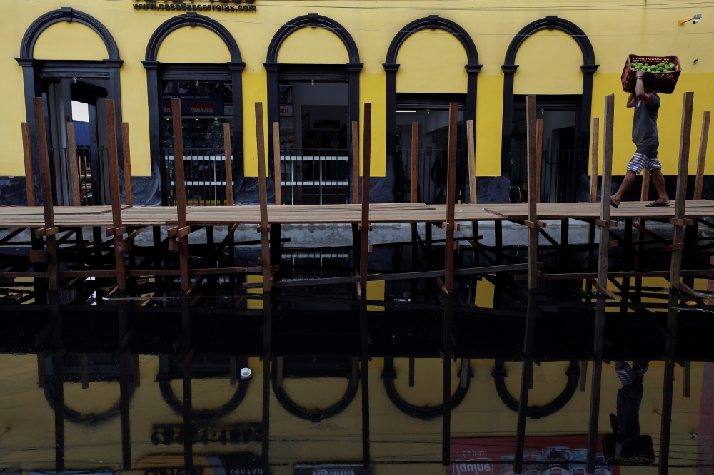 A man carries a box with oranges as he walks over wooden walkways installed by the city hall over a street flooded by waters from the Negro river in downtown of Manaus, in Amazonas State, Brazil May 17, 2021. REUTERS/Bruno Kelly