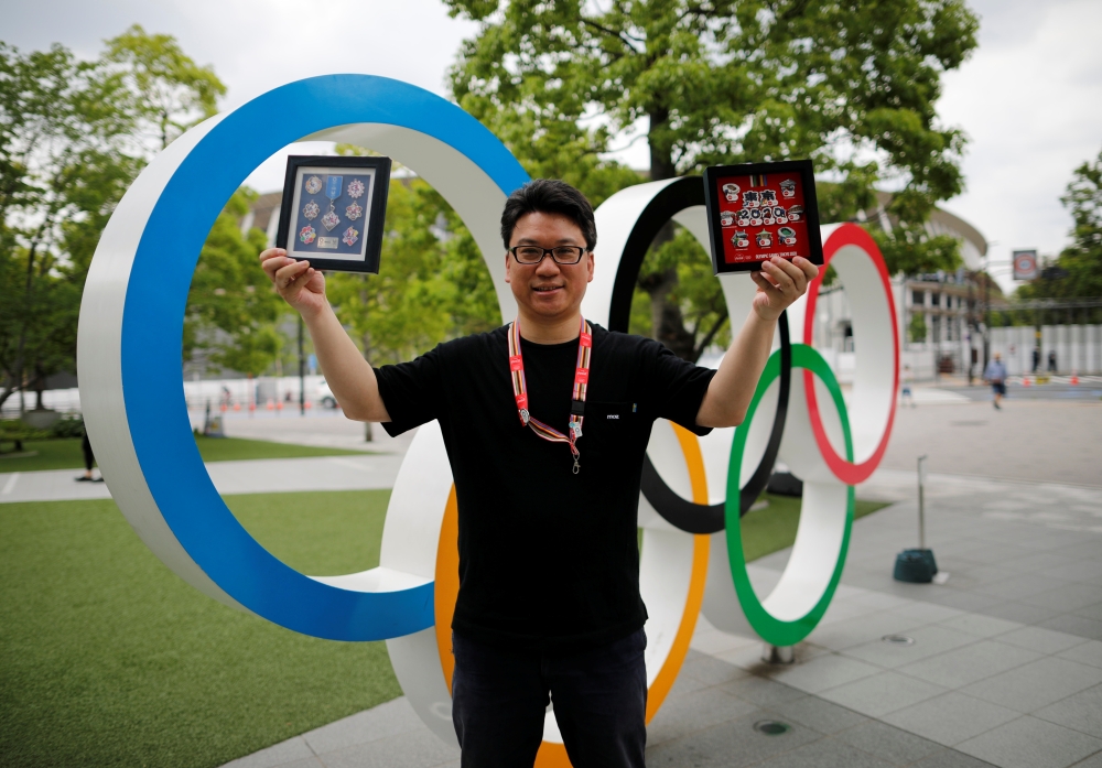Yoshiyuki Terajima (51), a pin collector based in Tokyo, shows his collection next to the Olympic rings monument in Tokyo, Japan June 13, 2021. Reuters/Issei Kato
 
