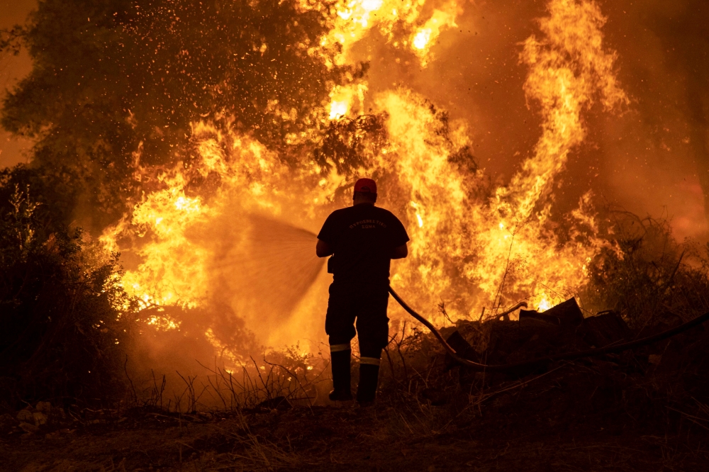 A firefighter tries to extinguish a wildfire burning in the village of Pefki, on the island of Evia, Greece, August 8, 2021. REUTERS/Nikolas Economou