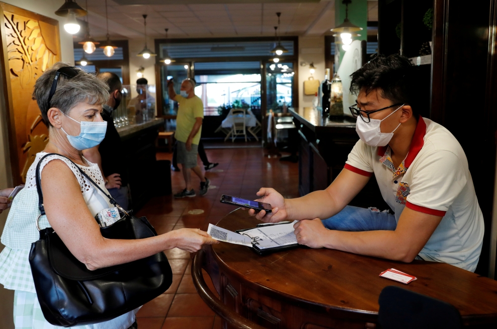 A woman has her Green Pass (health pass) checked before entering a pizzeria as Italy brings in tougher restrictions where a proof of immunity will be required to access an array of services and leisure activities, in Rome, Italy, August 6, 2021. REUTERS/R