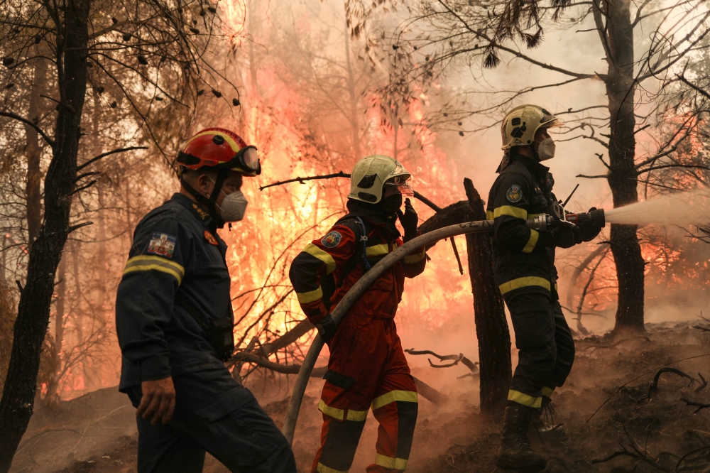 Two firefighters from Greece and one firefighter from Slovakia try to extinguish a wildfire burning in the village of Avgaria, on the island of Evia, Greece, August 10, 2021. REUTERS/Stelios Misinas