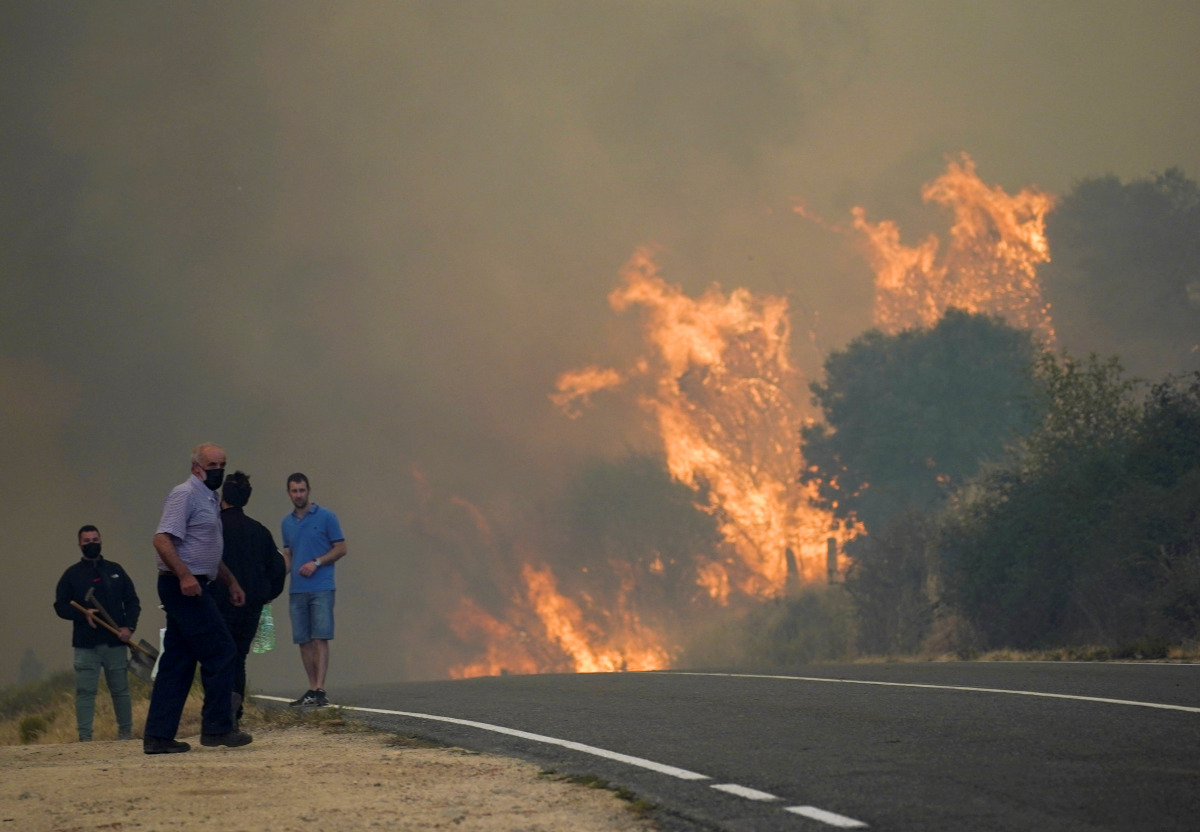 People stand on the road during a wildfire burning in the village of Navalmoral, Spain, August 16, 2021. REUTERS/Juan Medina
