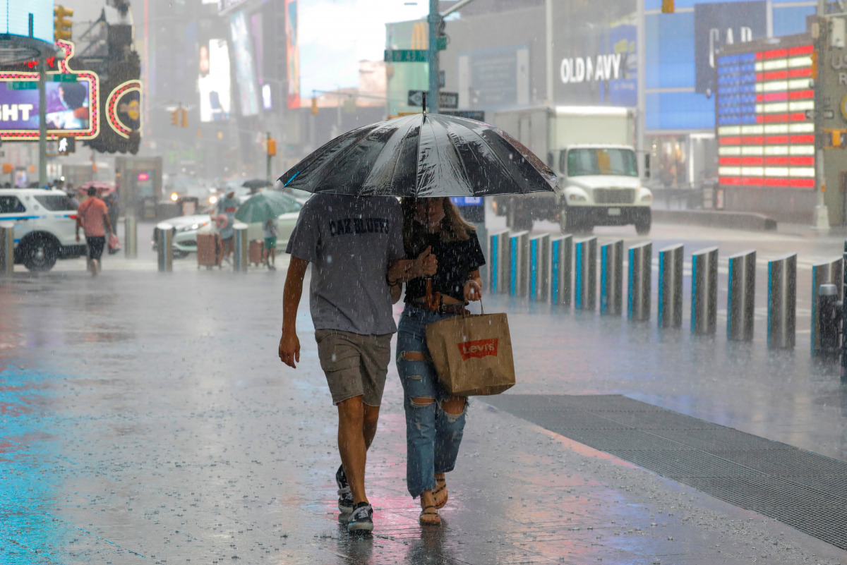 People walk through falling rain in Times Square as Tropical Storm Henri affects the region in Manhattan, New York City, U.S., August 23, 2021. REUTERS/Andrew Kelly
