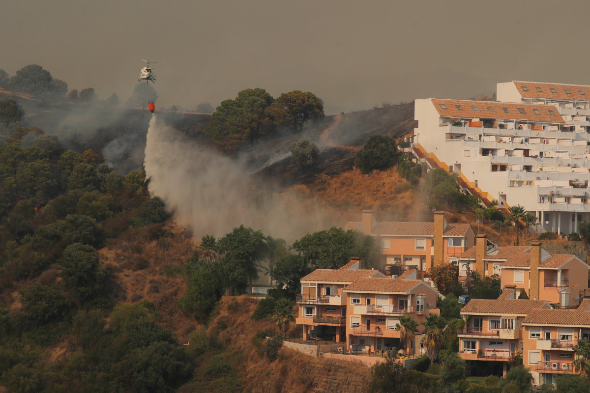 A helicopter makes a water drop over a wildfire burning near buildings on Sierra Bermeja mountain in Estepona, Spain, September 9, 2021. REUTERS/Jon Nazca
