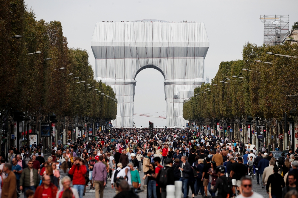 People walk near the Arc de Triomphe monument, fully wrapped as part of an art installation entitled 