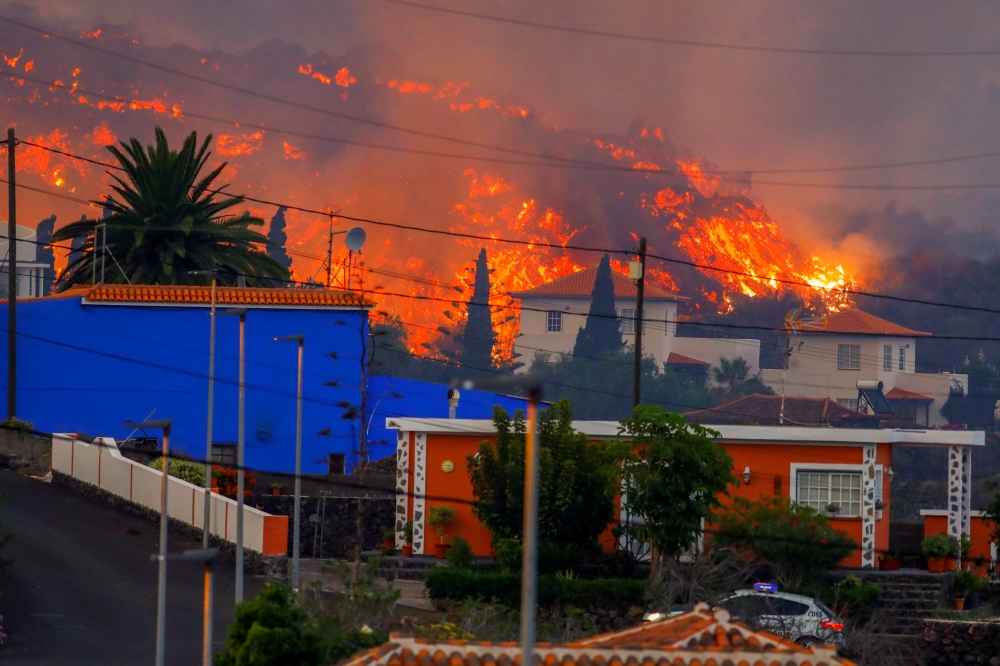 Lava flows behind houses following the eruption of a volcano in the Cumbre Vieja national park at Los Llanos de Aridane, on the Canary Island of La Palma, September 20, 2021. REUTERS/Borja Suarez