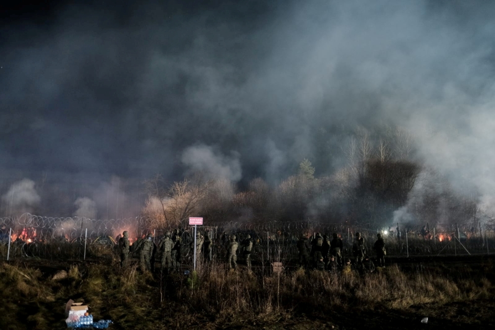 Polish service members stand guard next to a barbed wire fence on the frontier, as hundreds of migrants gather on the Belarusian side of the border with Poland in an attempt to cross it, near Kuznica Bialostocka, Poland, in this handout picture released by the Polish Defence Ministry, November 9, 2021. 