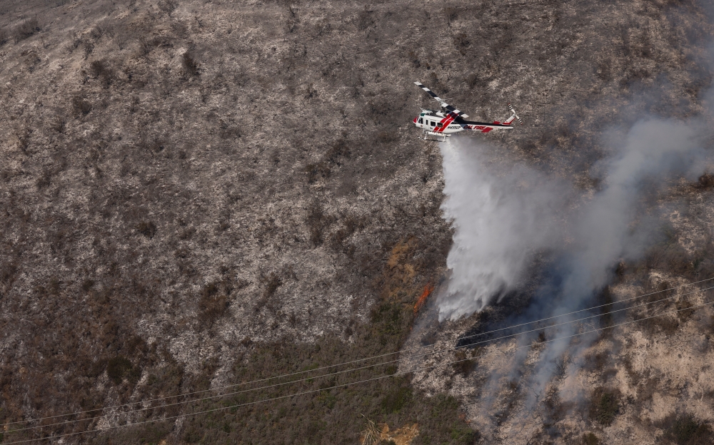 A Cal fire water dropping helicopter drops its payload on a hot spot as the Colorado fire burns near Big Sur, California, U.S. January 22, 2022. REUTERS/Peter DaSilva