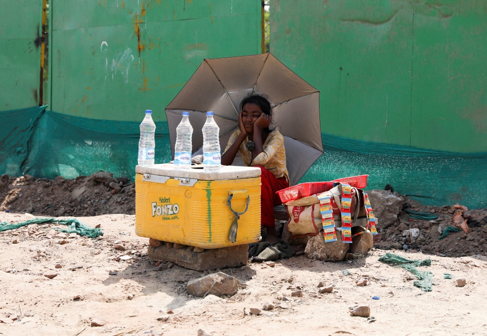  A girl selling water uses an umbrella to protect herself from the sun as she waits for customers on a hot summer day, in New Delhi, India, April 27, 2022. REUTERS/Anushree Fadnavis/File Photo