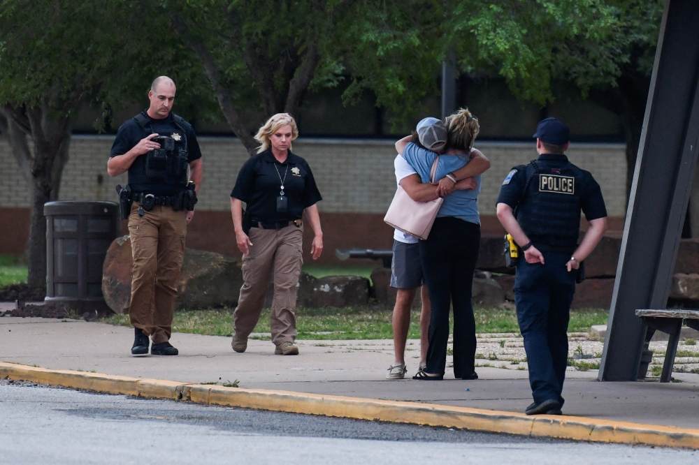 Police officers walk near people embracing at the reunion location, Memorial High School, where they wait to get more information after a shooting at the Saint Francis hospital campus, in Tulsa, Oklahoma, June 1, 2022. Reuters/Michael Noble Jr.