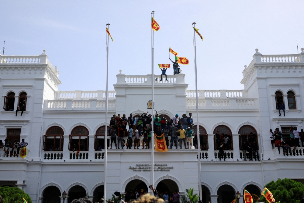 Protestors hold Sri Lankan flags as they stand on top of the office of Sri Lanka's Prime Minister Ranil Wickremesinghe, amid the country's economic crisis, in Colombo, Sri Lanka July 13, 2022. (REUTERS/Adnan Abidi)