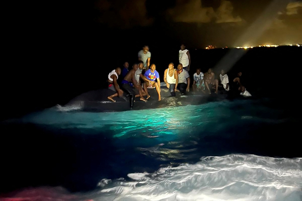 Survivors of a migrant boat that capsized perch on the overturned vessel off the coast of New Providence Island, Bahamas, July 24, 2022. (Royal Bahamas Defence Force/Handout via REUTERS)

