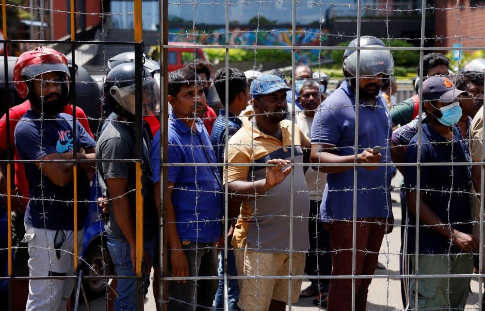 People stand behind a barbed wired gate to buy fuel at a Ceylon Petroleum Corporation fuel station, amid the country's economic crisis, in Colombo, Sri Lanka, July 26, 2022. (REUTERS/Dinuka Liyanawatte)