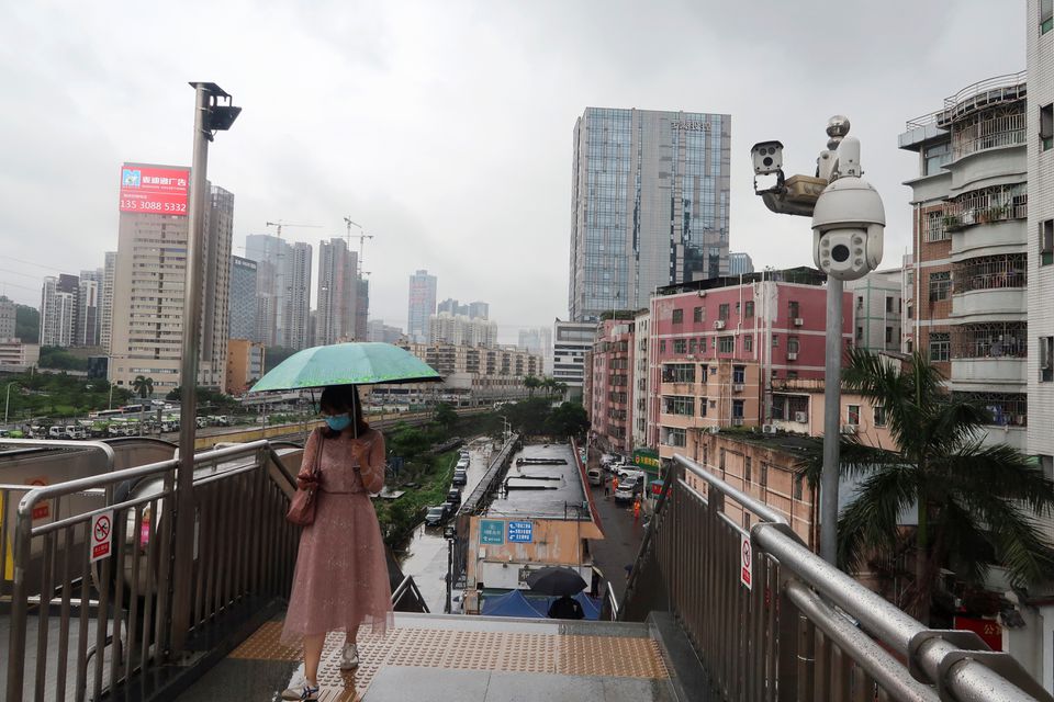 A woman holding an umbrella walks on a pedestrian bridge by surveillance cameras, near Caopu in Shenzhen's Luohu district, Guangdong province, China July 5, 2022. REUTERS/David Kirton

