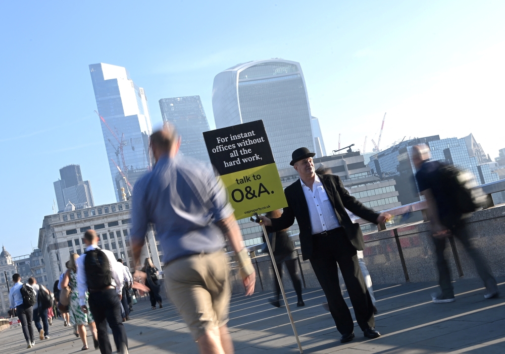 Workers pass by a sales person as they walk towards the City of London financial district, during the morning rush hour in London, Britain, September 8, 2021. REUTERS/Toby Melville/File Photo