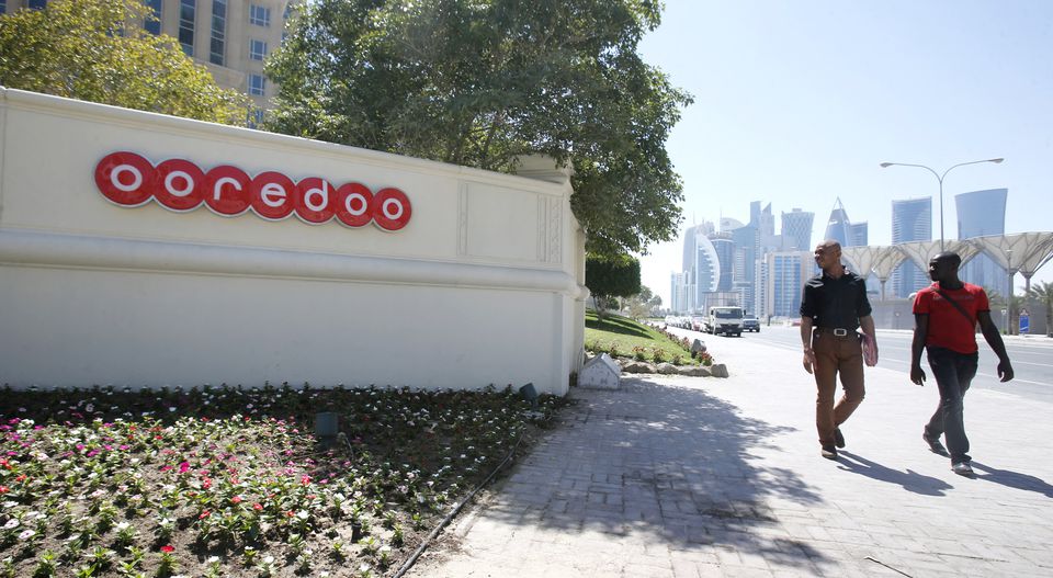 Men look at the logo of Qatar Telecom Ooredoo, formerly Qatar Telecom Qtel, as they walk past the company's head office in Doha March 16, 2013. REUTERS/Fadi Al-Assaad


