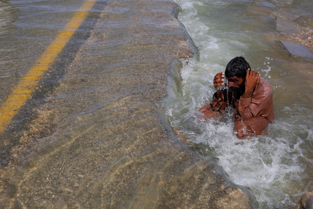 A displaced man cools off to avoid heat on flooded highway, following rains and floods during the monsoon season in Sehwan, Pakistan, on September 16, 2022. REUTERS/Akhtar Soomro 