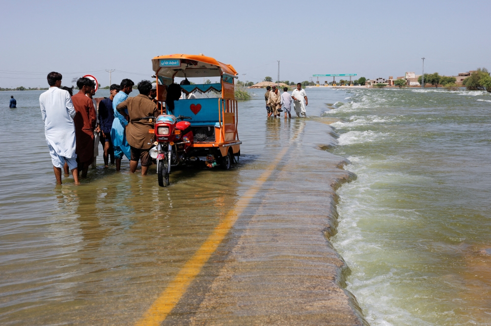 Displaced people stand on a flooded highway, following rains and floods during the monsoon season in Sehwan, Pakistan, on September 16, 2022. (REUTERS/Akhtar Soomro)