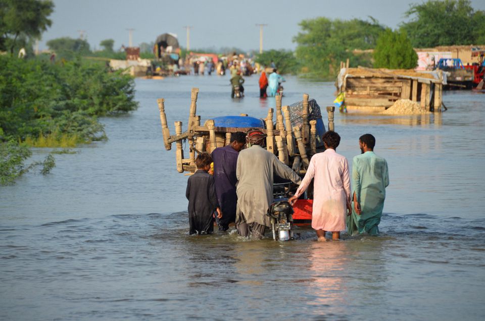 Men walk along a flooded road with their belongings, following rains and floods during the monsoon season in Sohbatpur, Pakistan, on August 28, 2022. (REUTERS/Amer Hussain)